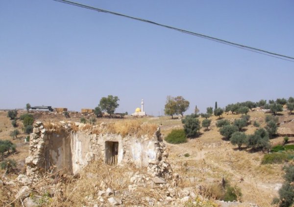 أنقاض المنازل القديمة، ومباني القرية التي أقيمت على أراضيها، نقلاً عن موقع فلسطين في الذاكرة