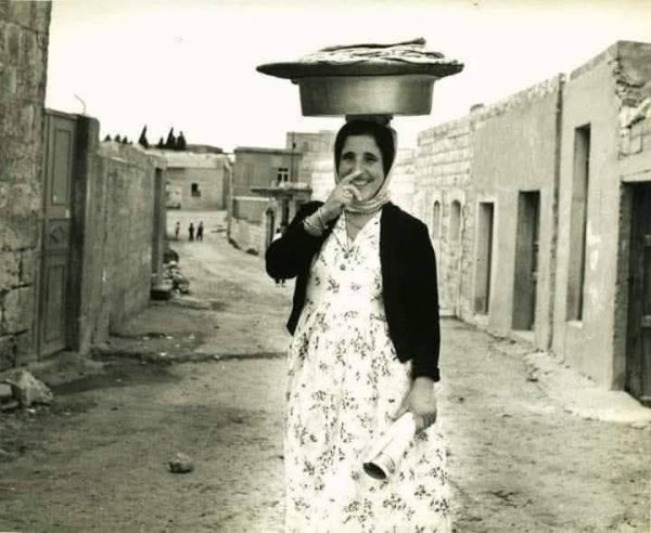 ام الياس في قرية عسفيا ، قضاء حيفا/ فلسطين   تحمل خبز الصاج،  عام 1950م